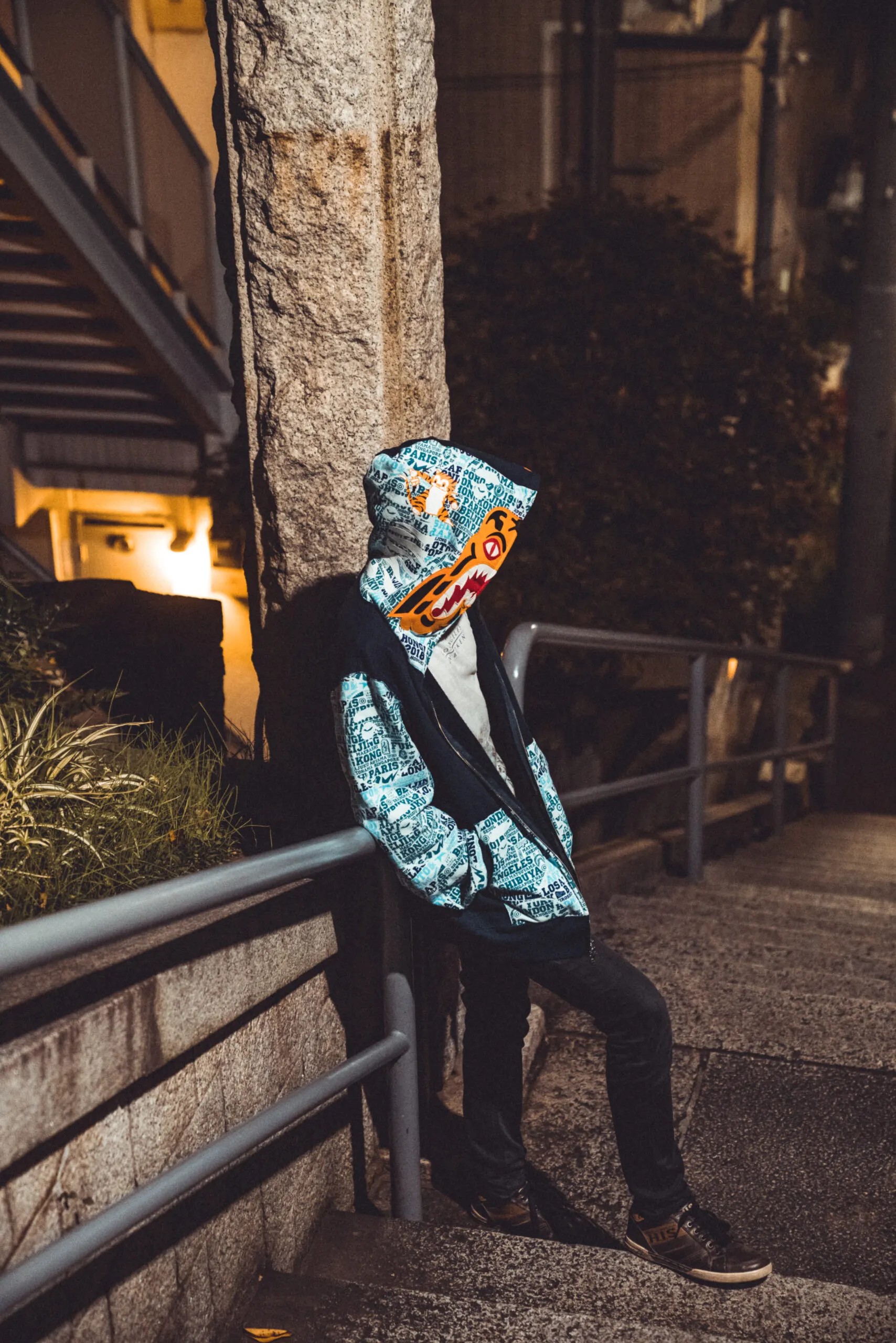Person in a patterned hoodie and mask leaning on a railing